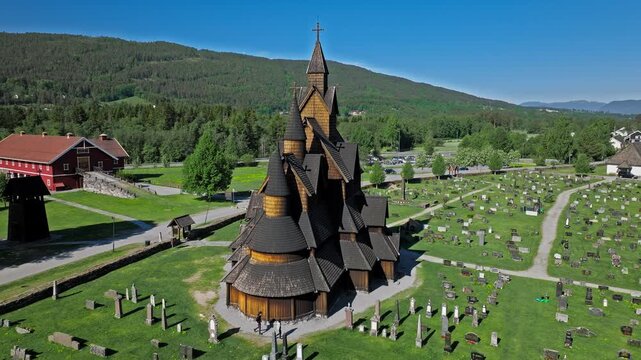 Low orbit drone shot of Heddal Stave Church Replica at Norsk Folkemuseum Oslo. Summer daylight tourism view capturing carved wood, burial ground and Nordic heritage scene.