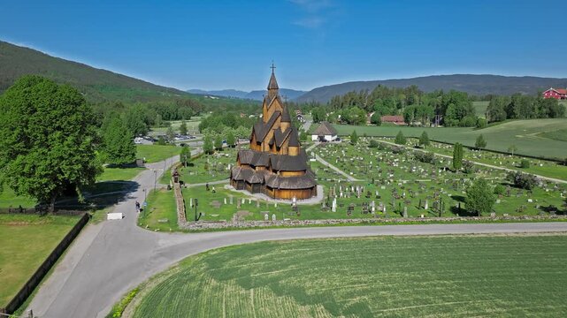 Drone aerial of Heddal Stave Church cemetery near Norsk Folkemuseum exhibit Norway. Sunny summer morning travel shot showing wooden towers, gravestones and green fields.
