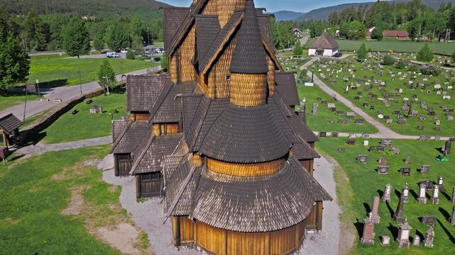Drone aerial orbit of Heddal stave church featuring stave church and cemetery on Bygdoy. Sunny summer morning tourism scene showing wooden towers, footpaths and fjordside heritage mood.
