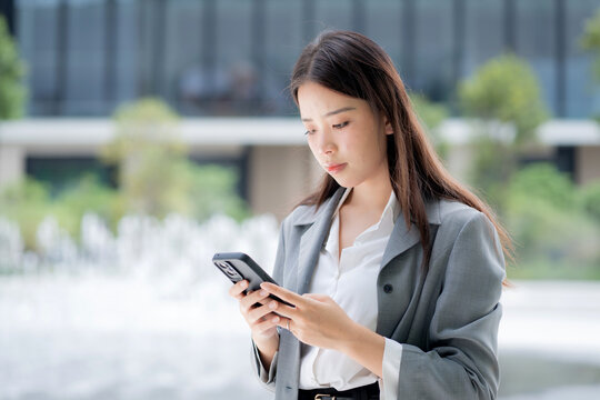 Young asian businesswoman using chatbot or AI message on smartphone outdoors in city, business woman chat on smart phone with AI assistant in urban, artificial intelligence, technology and business. - Powered by Adobe