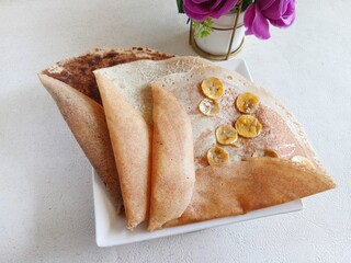 three pieces of traditional Indonesian leker crepes. Each crepe features different fillings such as chocolate and banana slices. Arranged artistically in a semi-circle shape on a clean white surface. 