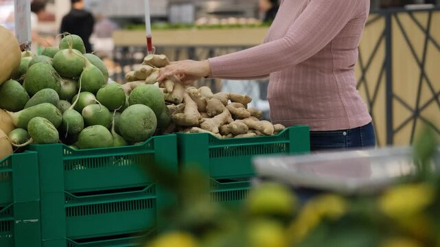 Woman selecting fresh ginger near radish stand in supermarket, checking aroma and texture, vegan food and organic lifestyle concept
