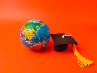 Miniature graduation cap and a small globe against a orange background