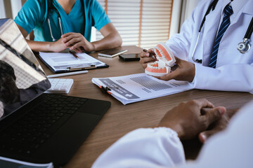 Dental professionals discussing treatment plans with a tooth model and medical documents during a meeting.