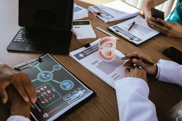 Dental professionals discussing treatment plans with a tooth model and medical documents during a meeting.