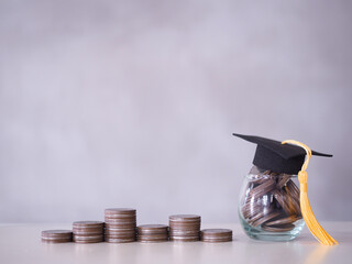 Glass bottle with graduation hat and stack of coins. The concept of saving money for education,...