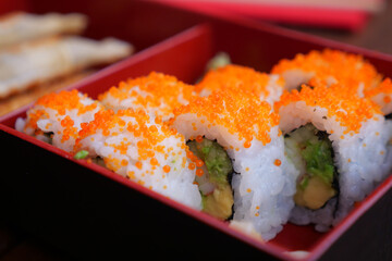 Sushi rolls with orange toppings served in a red box