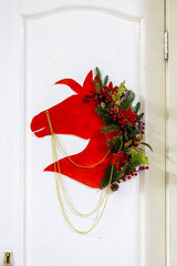 Christmas and New Year composition. Red paper Horse head wreath on white wooden door. Modern style. Close up. Selective focus. Copy space. Vertical