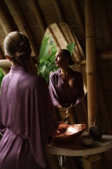 A woman stands near a mirror in a bamboo-designed eco bathroom with warm natural light and tropical details