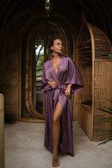 Fototapeta premium A woman in a purple robe stands in a bamboo corridor with handcrafted walls and tropical greenery in the background