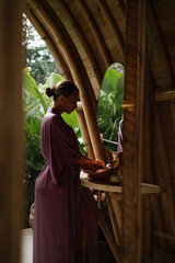 A woman washes her hands in a bamboo eco bathroom with natural light and tropical greenery visible outside