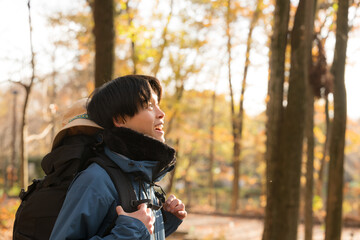 逆光の秋冬の紅葉の山を登山をする景色を見上げる若い男性 アウトドアのお出かけやレジャーのイメージ 横顔