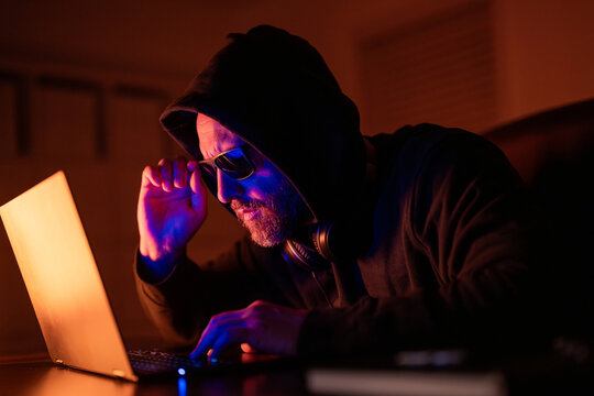 Cyber attack. Cyber criminal and stolen financial data. Digital money thief. Hacker programmer in hoodie at office laptop, gaming. Hacker attack. Hacker gamer at night in office. Midnight hacker - Powered by Adobe