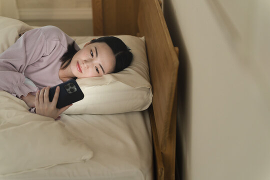 布団の中でスマートフォンを操作する若い女性　ライフスタイルイメージ