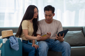 Young couple at home is planning a vacation trip and packing clothes, accessories into suitcases....