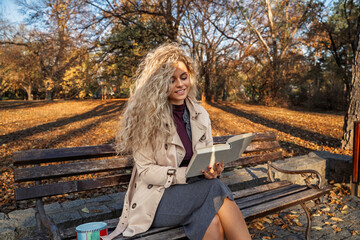 Beautiful curly hair girl reading a book in the park on the bench, beautiful fall day 