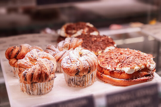 Fresh confectionery in the bakery window in close-up - brown muffins and muffins with powdered sugar and swirl dough, sweet rolls with chocolate cream and other desserts. High quality photo