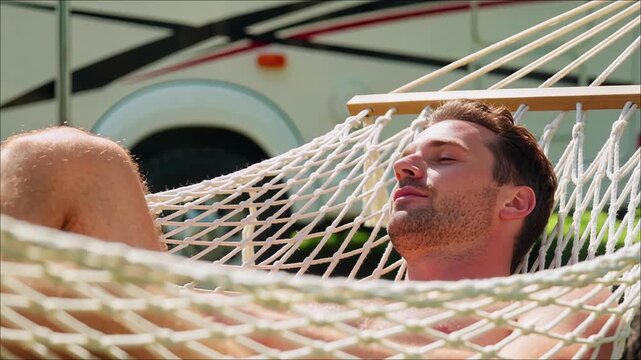 Young man relaxing in a woven rope hammock outdoors with an RV vehicle visible in the background