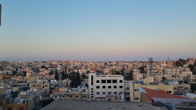 Panoramic skyline view over Madaba, Jordan, with evening sun illuminating rooftops and the city stretching across rolling hills toward the distant horizon