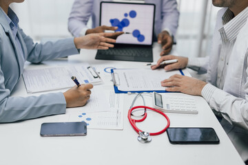 Medical professionals and administrators collaborating on medical data analysis with tablets and paperwork, calculating costs amidst stethoscopes and smartphones.