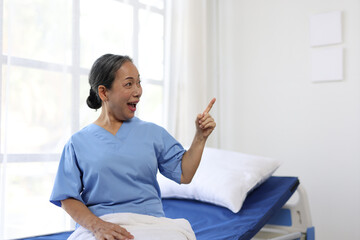 Elderly woman in a hospital gown sitting on a bed, raising her arms in joyful celebration of recovery and renewed health, radiating positivity and strength in the moment.