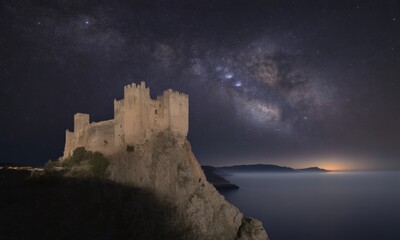 Ancient castle atop a cliff, bathed in moonlight, with a vibrant Milky Way