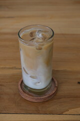 Chilled iced coffee served in a tall ribbed glass with ice cubes, placed on a wooden table with a soft blurred background.