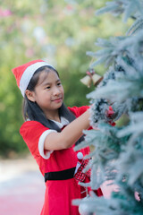 young woman dressed in a festive red Christmas outfit smiles softly. standing among beautifully decorated holiday trees.