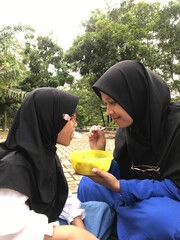 Mother in Hijab Feeding Her Young Daughter Outdoors
