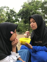 Hijab-Wearing Mother Feeding Her Child in an Outdoor Setting