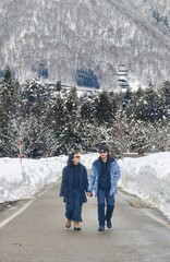 ​A couple walks hand-in-hand down a snow-covered mountain road, flanked by deep snowdrifts and a...