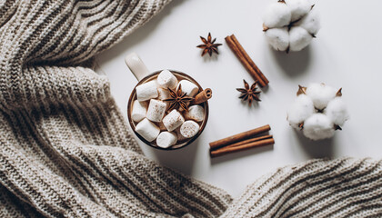 Fototapeta premium Comforting hot chocolate with marshmallows and spices, artfully styled with cotton bolls and a knitted blanket on a white background, creating a cozy autumn and winter ambiance