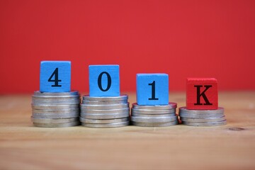 Stacks of coins support blue and red blocks forming '401K', symbolizing retirement savings and financial planning. Red background. emphasizes financial security, investment, and future wealth.