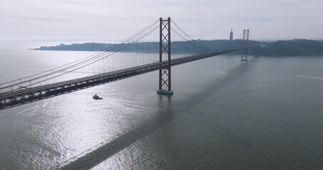 Cinematic aerial drone view of the red 25th April suspension bridge over the Tagus river in Lisbon, Portugal, with a single car crossing before a running event