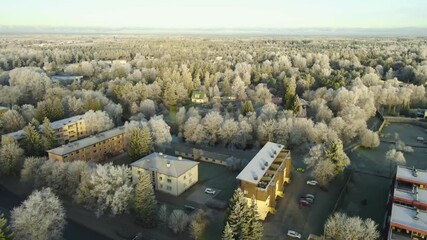 Aerial drone video orbiting and flying above a small urban town during winter sunny morning with trees and rooftops covered in hoar frost and white fluffy snow and ice. Horizon in the back, apartments - Powered by Adobe