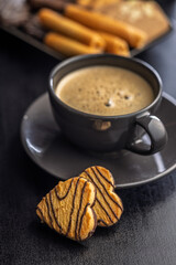 Heart shaped cookie and coffee cup on black table.