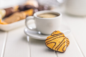 Heart shaped cookie and coffee cup on white table.