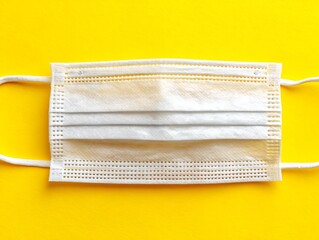 A close-up view of a medical face mask with white elastic straps set against yellow