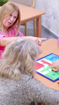 Elderly women and caregivers playing Parcheesi at nursing home