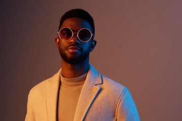Fototapeta premium Stylish male model wearing sunglasses and a light coat, showcasing modern fashion against a colorful backdrop, exuding confidence and charisma