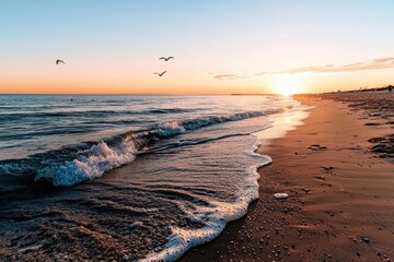 Peaceful beach at sunset with gentle waves rolling onto sandy shore and birds flying above, creating calm and serene coastal atmosphere