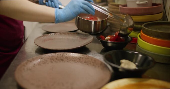 Ladling food. Portioned dish. Chef pouring hot red liquid meal in bowls standing row. Serving borsch on restaurant kitchen interior table.