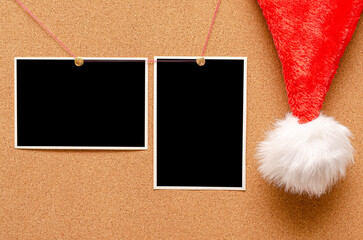Blank photos are pinned to the board. Santa's hat on a cork board.