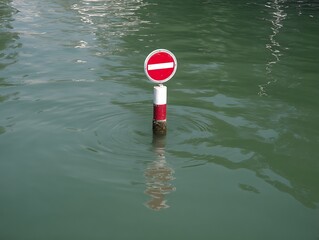 A no-entry road sign stands in murky water with circular ripples emanating outwards