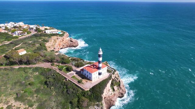 Drone footage of a black and white striped lighthouse on a cliff near Portocolom.