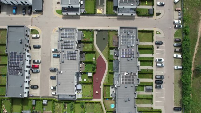 Direct overhead view of modern residential buildings with solar panels, private gardens, parking rows, and a winding pedestrian path forming a geometric layout.