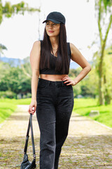 Young woman walking in a sunny park wearing casual black outfit and holding a small bag