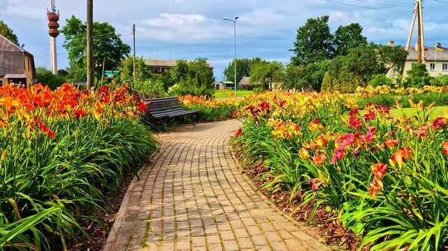 Colorful flower-lined brick path curving through public park with benches in summer