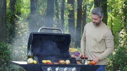 Smoke from barbeque with grilled beef. Man relaxing on picnic barbeque by nature. Middle-aged man cooking meat on barbeque grill. Backyard barbeque.