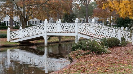 A white wooden bridge over a small waterway, framed by autumn trees & buildings